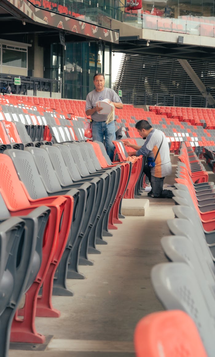 services-01 Two workers cleaning empty stadium seats, ensuring cleanliness before events.