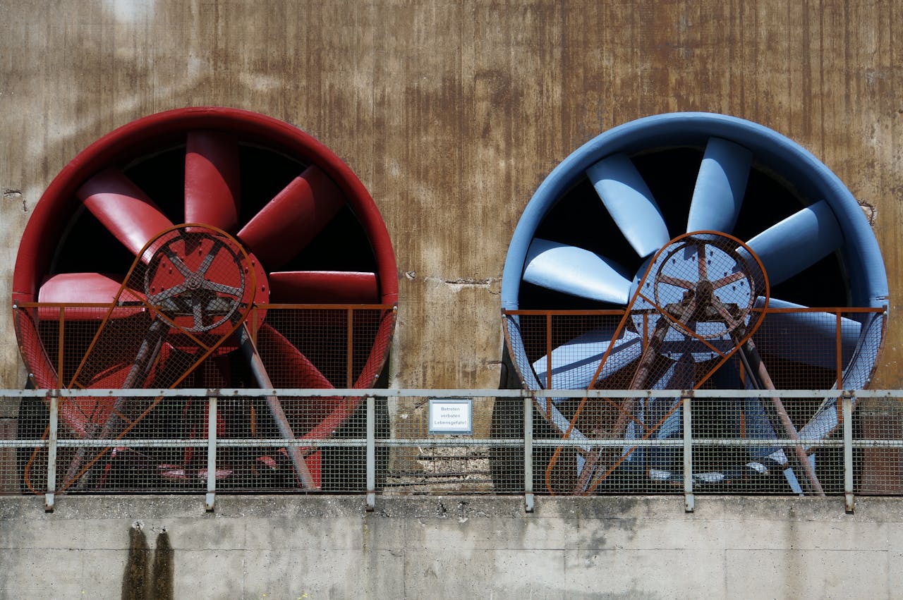 hero-img-01 Close-up of large red and blue industrial fans on a rustic wall showcasing machinery and ventilation.