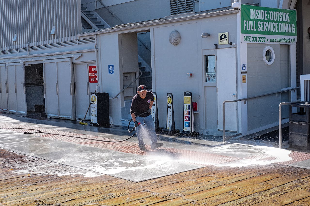about-01 A worker uses a pressure washer to clean a sidewalk outside a dining facility.